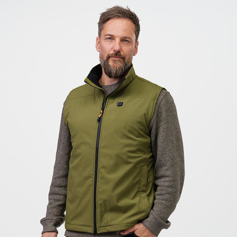 En mand bærer en grøn NordicHeat-varmevest over en grå trøje i en neutral indendørs setting.