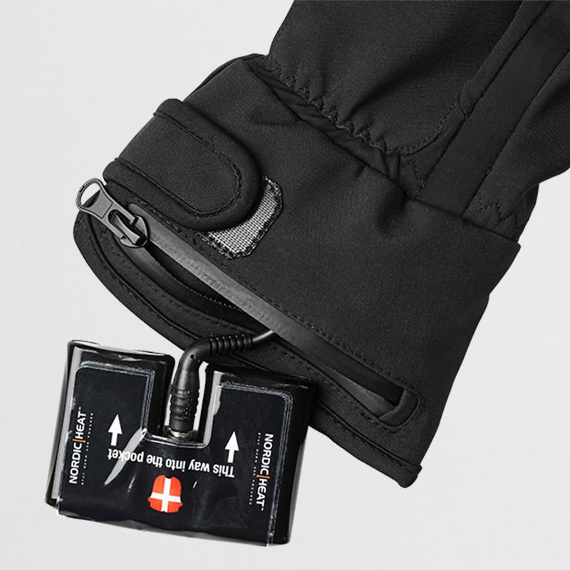 Sort handske med indbygget varmesystem fra NordicHeat. Batteripakke placeret i lynlåslomme med tekst “This way into pocket” og “NordicHeat” synlig.